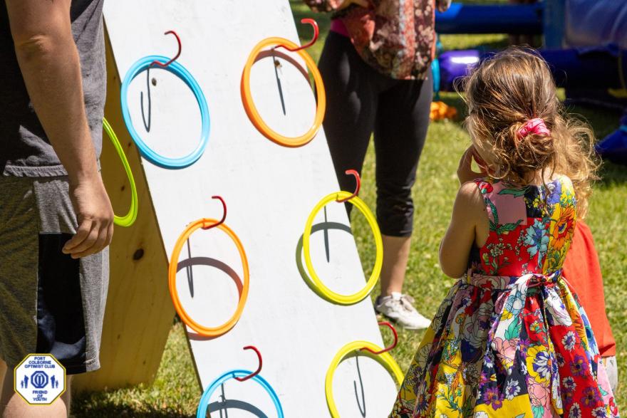 A game setup with a target board and colourful rings, children interacting outdoors.