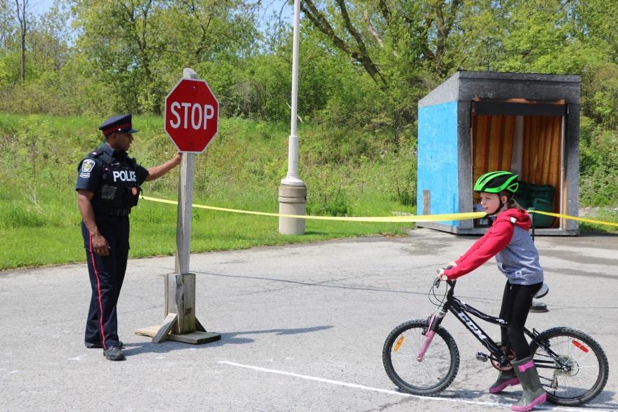 A police officer holds a stop sign while a cyclist pauses nearby in a park setting.