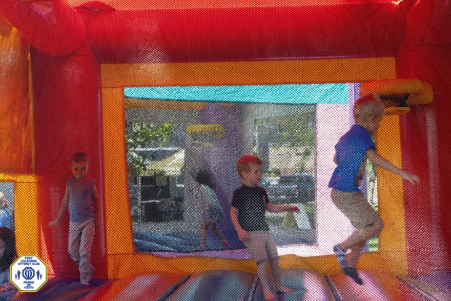 Three children play and jump inside a bright, colourful bouncy castle.