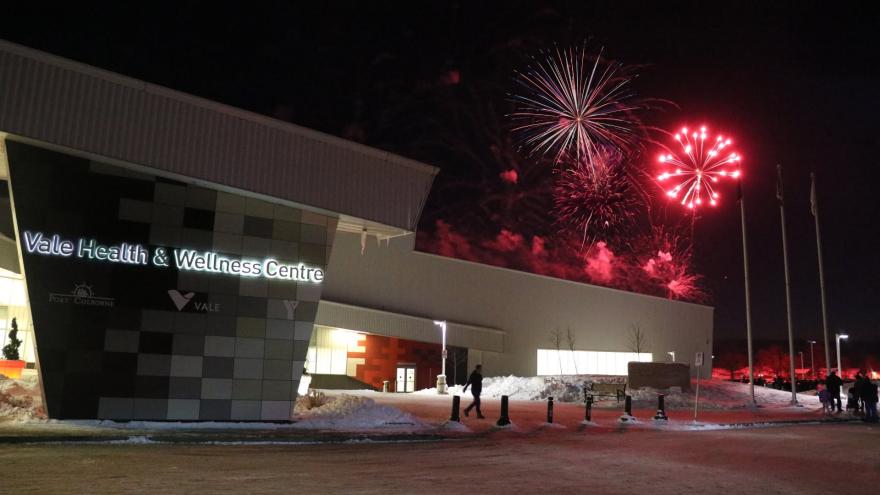 Fireworks illuminate the night sky above a modern health facility, with snow on the ground.