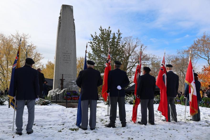A group of individuals stands in front of a monument, holding flags, in a snowy setting.