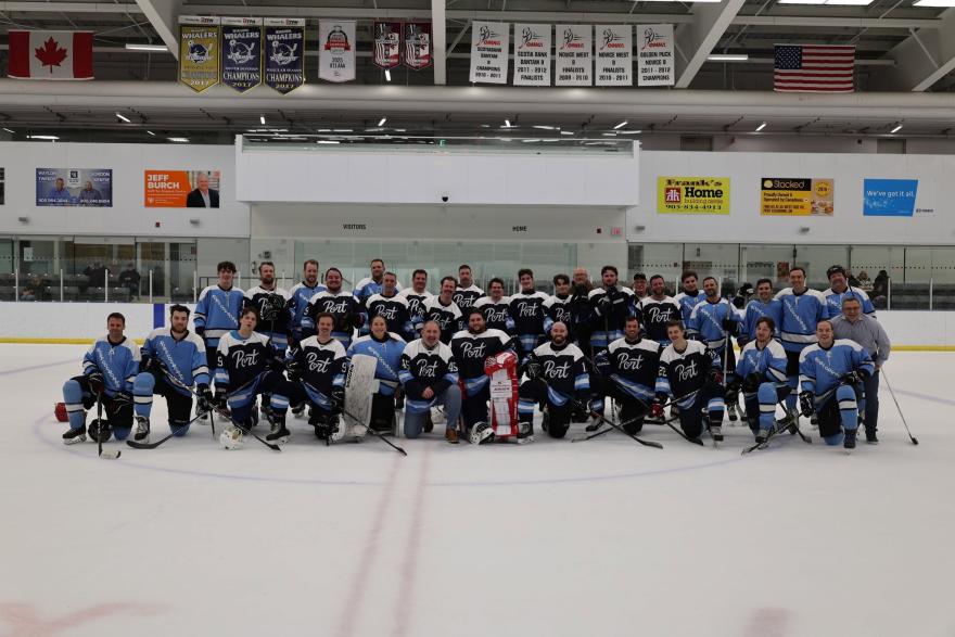 Large group of hockey players posing on ice rink, some in blue jerseys, others in black.