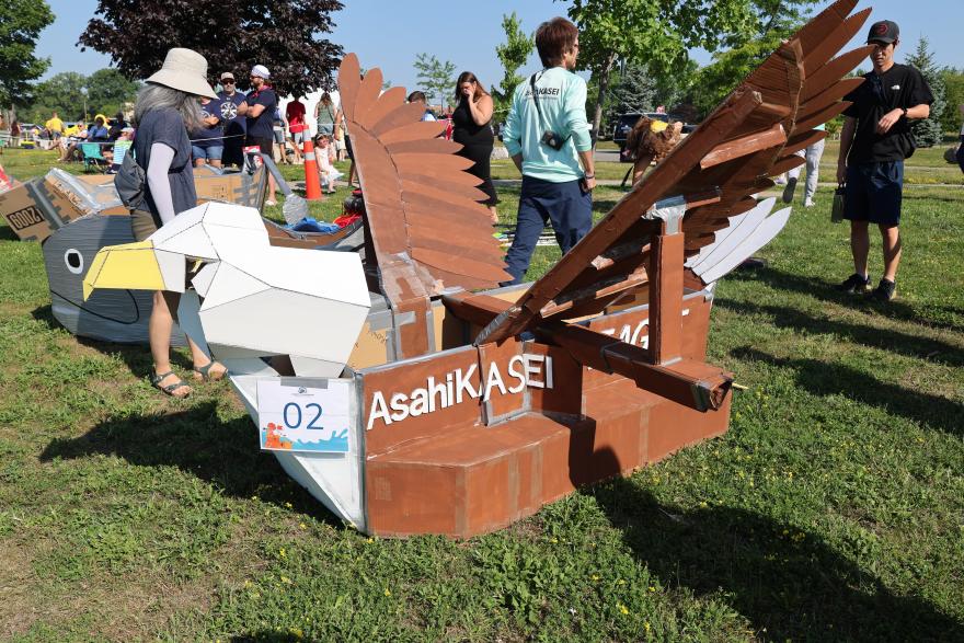 A large, artistic eagle-shaped float made of cardboard, set on grass with people nearby.