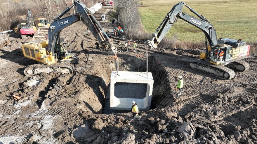 Excavators working on a construction site, lifting a large concrete structure from a pit.