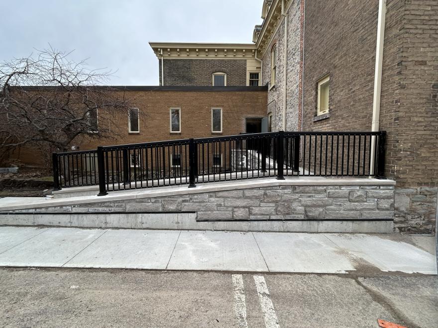 A ramp with a railing leading to a brick building, surrounded by a paved area.
