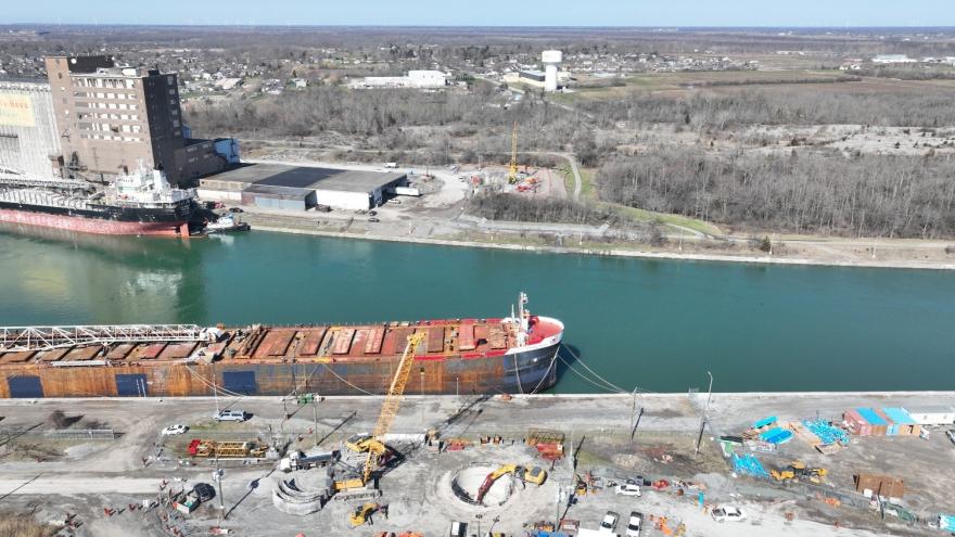 Aerial view of a shipping port with vessels, buildings, and a river surrounded by dry land.