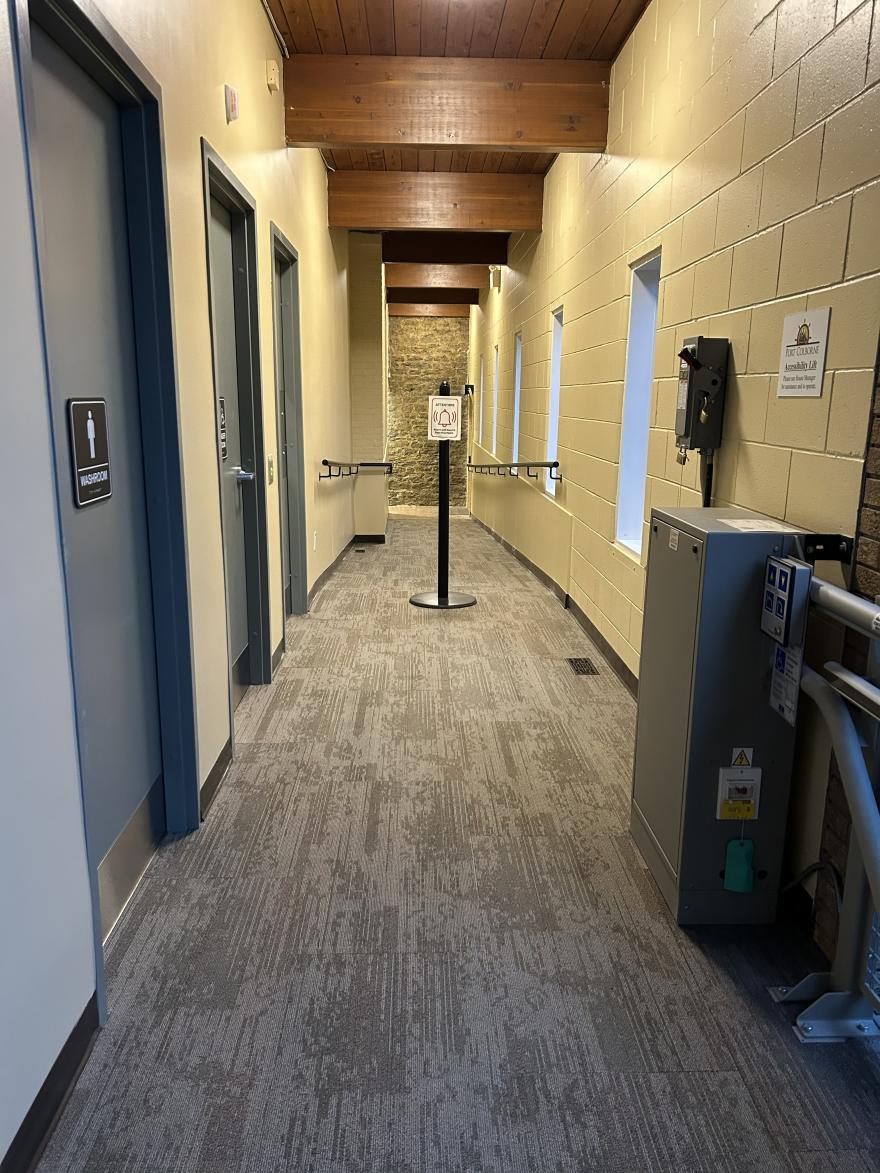 Hallway with doors on either side, a post with a sign in the centre, and windows along the wall.