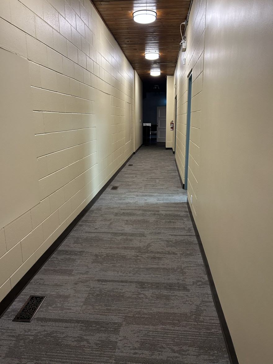 Narrow hallway with beige walls, carpeted floor, and overhead lighting.