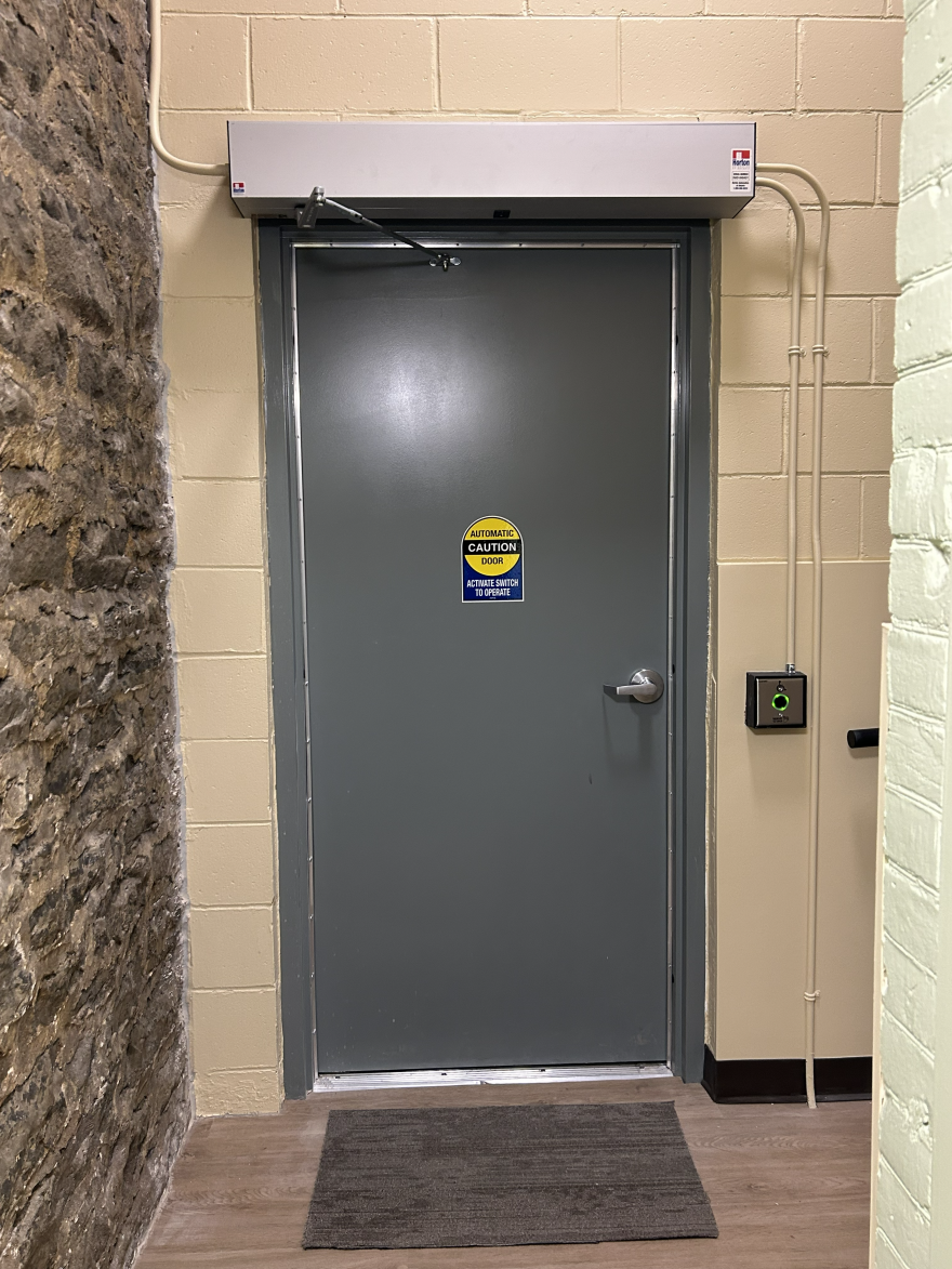 A grey door with a security system and a mat, surrounded by stone walls.
