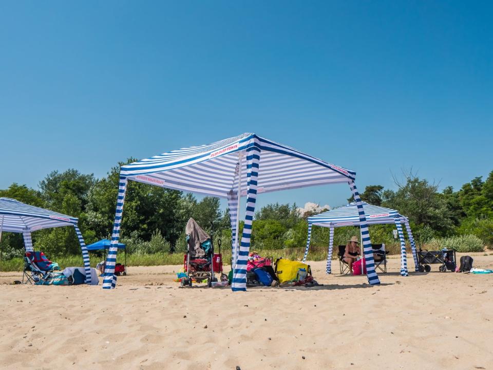 Beach scene featuring striped canopies and various chairs under a clear blue sky.