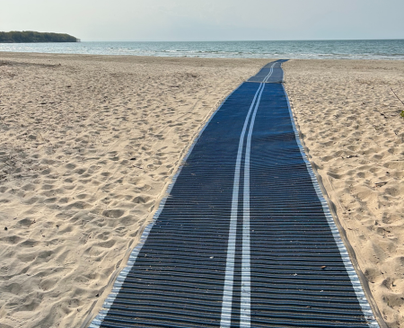 A blue mat stretches across sandy beach leading to the calm ocean.