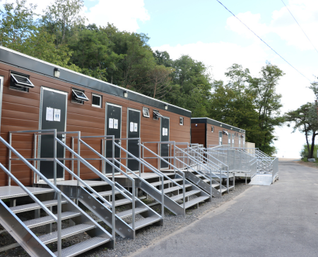 Row of modern wooden cabins with accessible steps, surrounded by greenery and a cloudy sky.