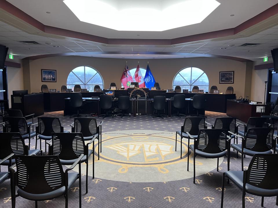 Council chamber with empty chairs, flags, and a circular decorative floor design.