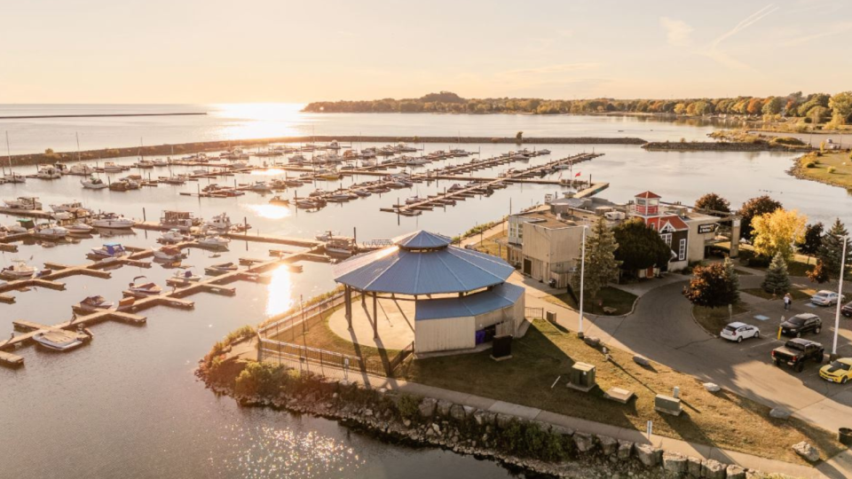 Aerial view of a marina at sunset, featuring boats, a gazebo, and shoreline trees.