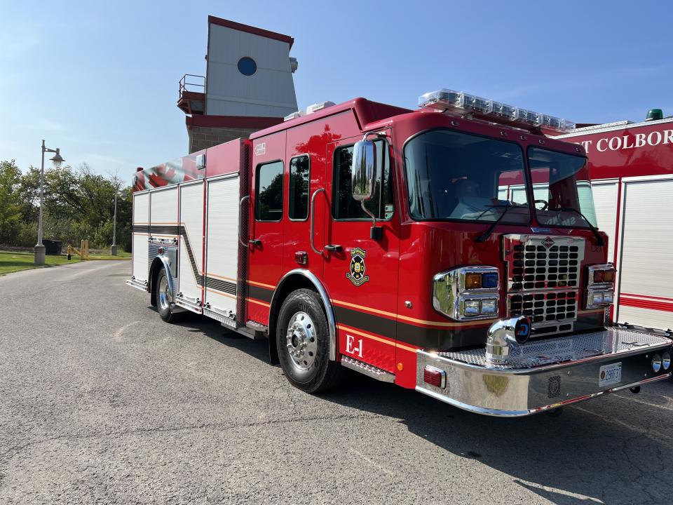 A bright red fire truck parked on asphalt with a fire station in the background.