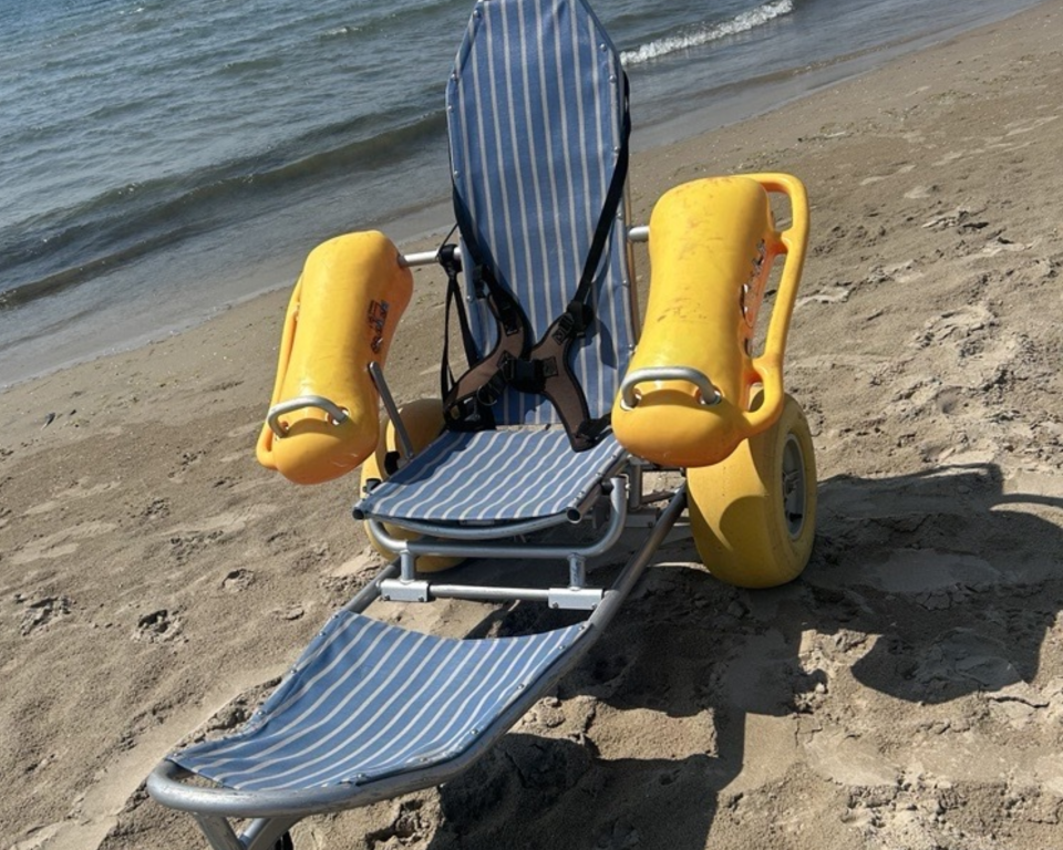 A beach wheelchair with yellow flotation devices near the water's edge.