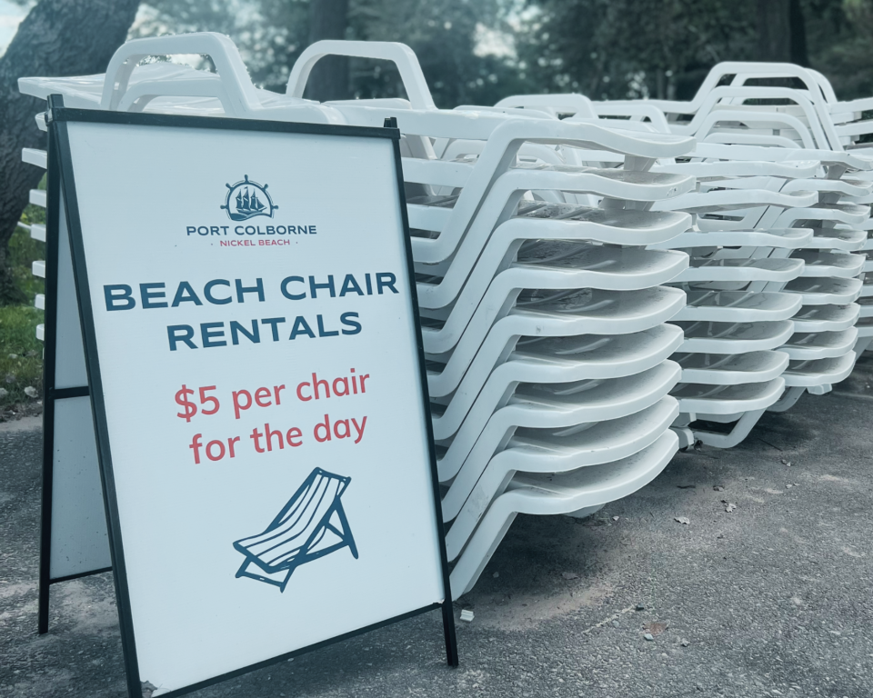 White beach chairs stacked beside a rental sign for $5 per chair per day.
