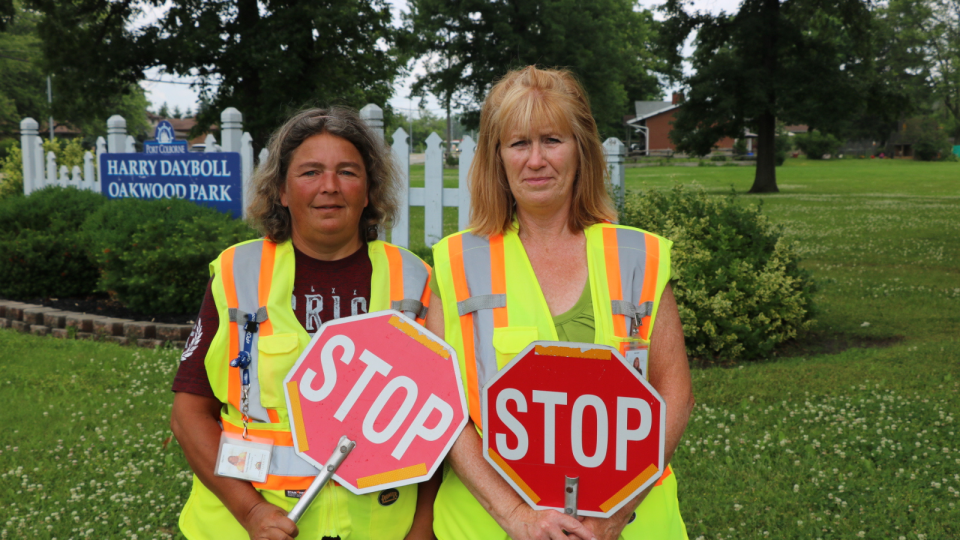 Two individuals in reflective vests holding stop signs in a grassy area.