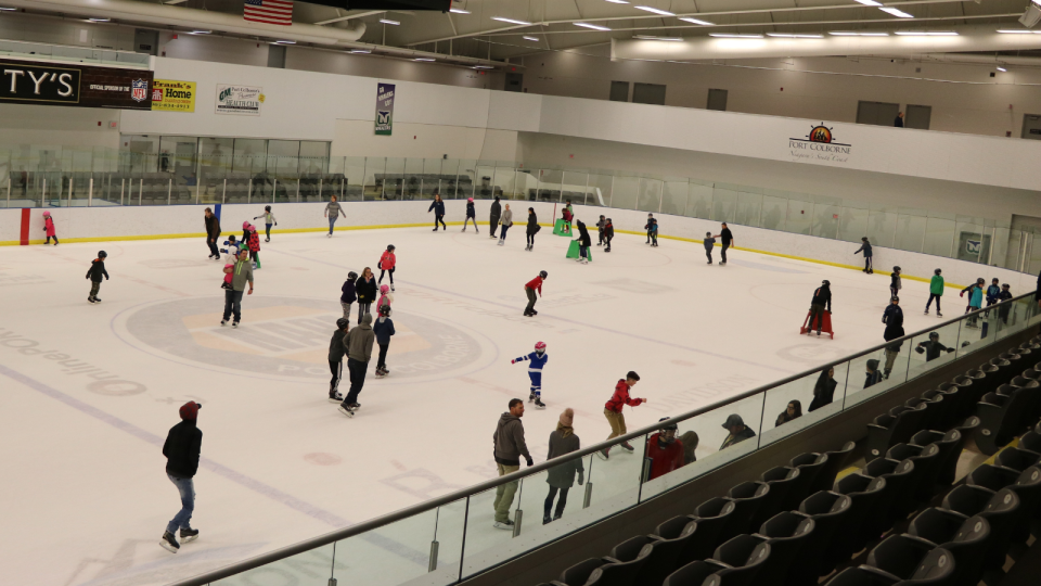 A busy ice rink with many skaters of various ages enjoying recreational skating.