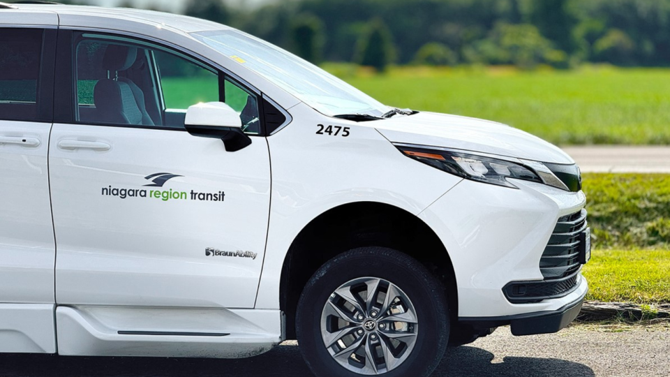 White van with "Niagara Region Transit" logo parked beside a green field.
