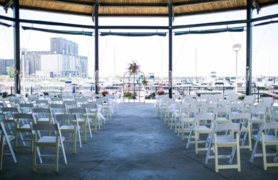 White folding chairs arranged in a semicircle under a gazebo, with a waterfront view.