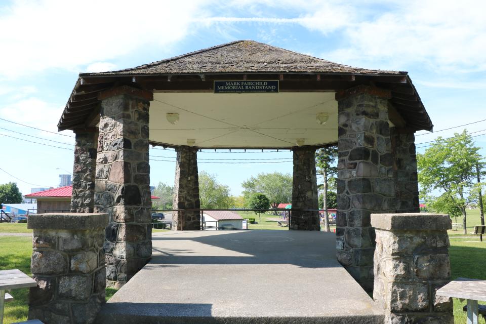Stone pavilion with a grassy park in the background under a clear blue sky.