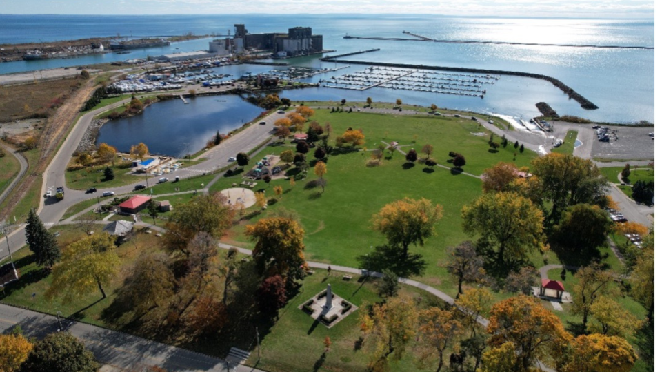 Aerial view of a park with colourful trees beside a lake and marina under a bright sky.