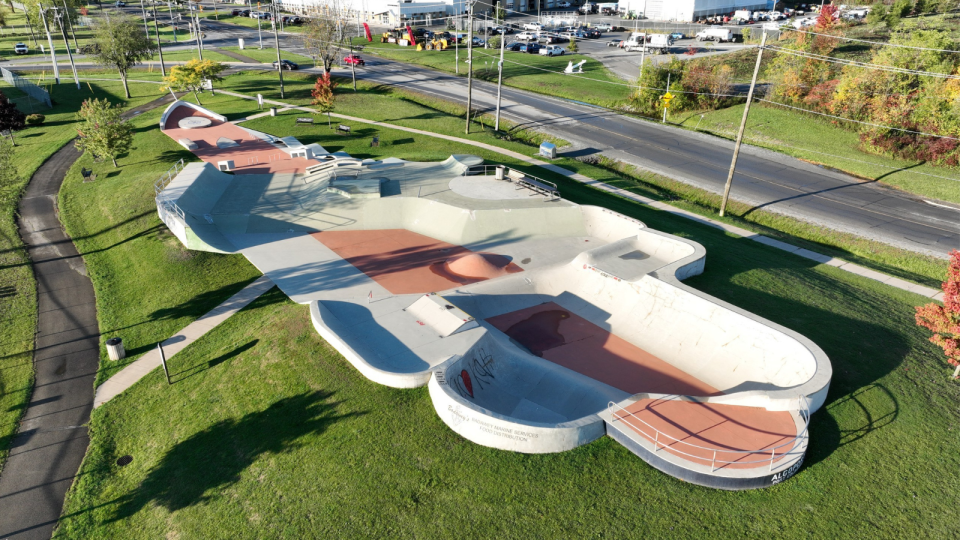 Aerial view of a skatepark with ramps and smooth surfaces, surrounded by green grass.