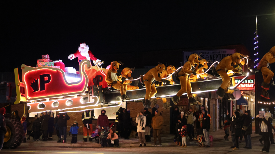 Brightly lit parade float with Santa and reindeer, surrounded by a crowd at night.