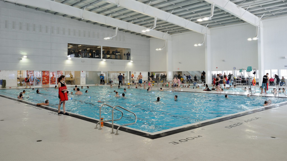 Indoor swimming pool with various people swimming and relaxing around the water.