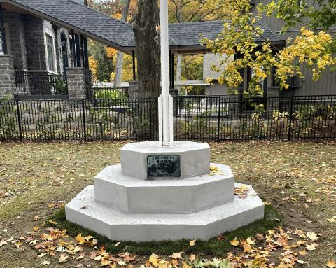 A stone monument with a flagpole, surrounded by autumn leaves and a park setting.