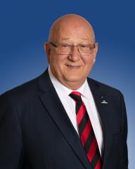 A smiling individual in a suit with a red and black striped tie against a blue background.