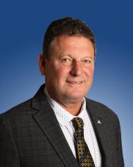A person in a suit with a patterned tie, smiling against a blue background.