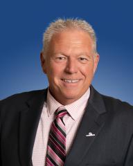 Portrait of a smiling person wearing a suit and tie, with a blue background.