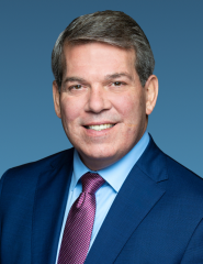 Formal portrait of a person in a blue suit and pink tie with a neutral background.