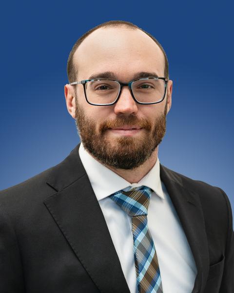 Professional portrait with a person in formal attire, smiling against a blue background.