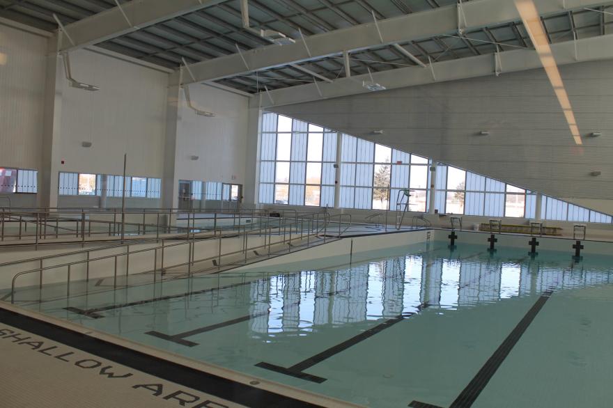 Bright indoor swimming pool with empty lanes and large windows allowing natural light.