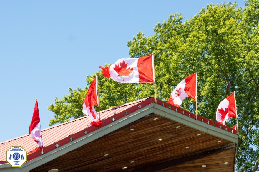 Canadian flags flutter atop a wooden building against a clear blue sky.