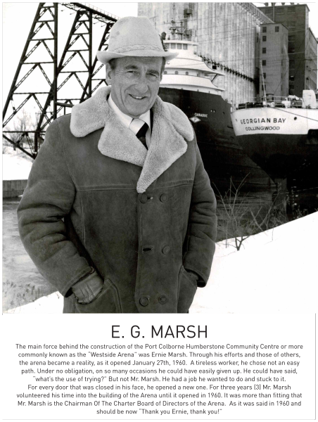 Black and white portrait of a man wearing a hat and coat, with boats and structures in the background.