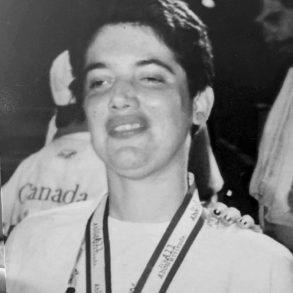 A smiling individual wearing a medal and a white shirt, with a blurred crowd in the background.