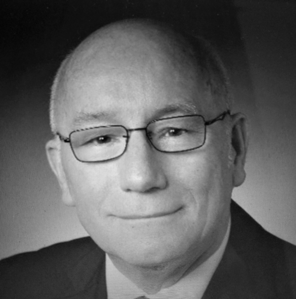 Black and white portrait of a smiling person wearing glasses and a suit.