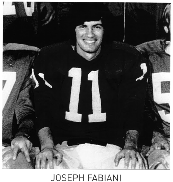 Black and white photograph of a smiling athlete in a football jersey, seated among teammates.