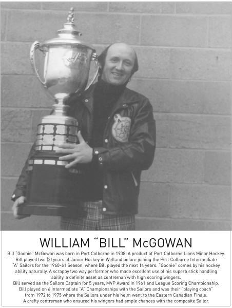 A person smiles while holding a large trophy, wearing a leather jacket against a grey wall.