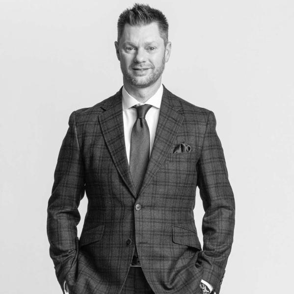 A person in a checked suit standing confidently against a plain background.
