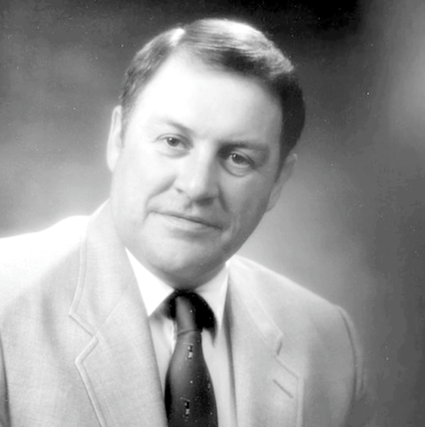 Black and white portrait of a person smiling, wearing a light-coloured suit and tie.