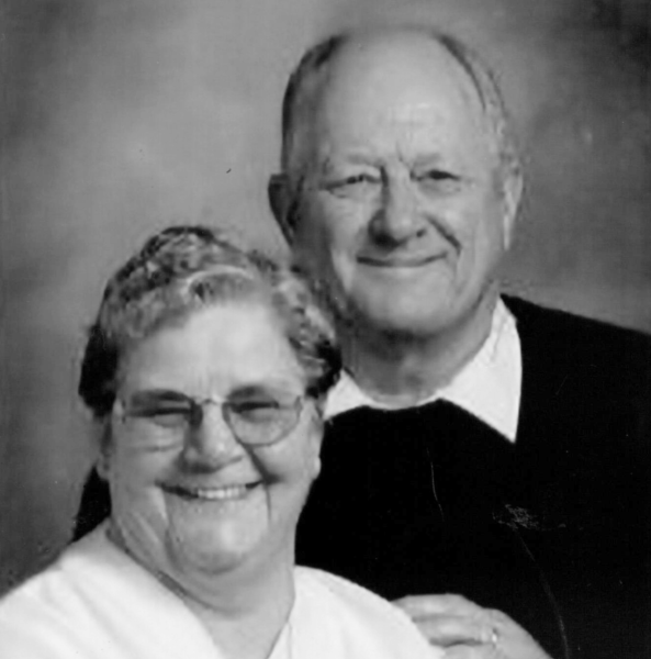 Smiling couple posing closely against a blurred background in black and white.
