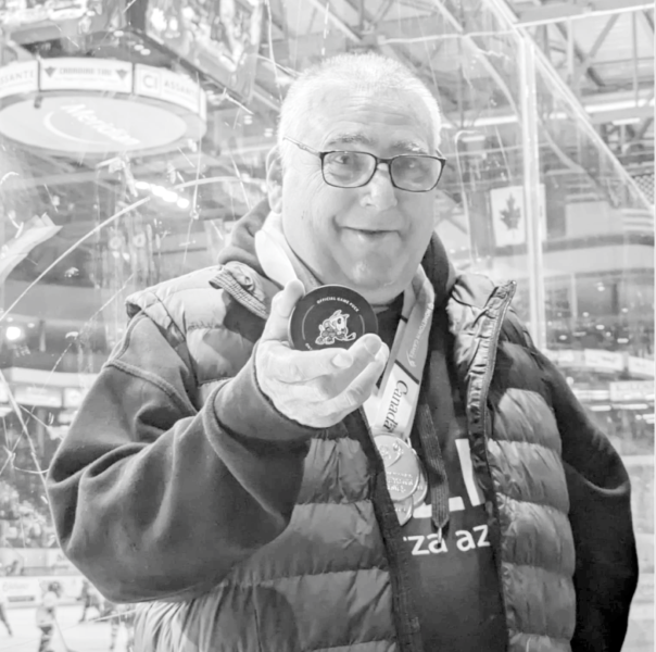 A smiling person holding a hockey puck inside a sports arena.