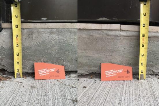 A measuring tape stands next to an orange marker on a concrete surface with a wall in the background.