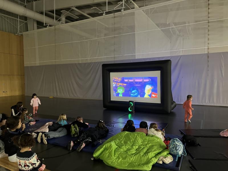 Children seated on the floor watching a cartoon on a large inflatable screen.