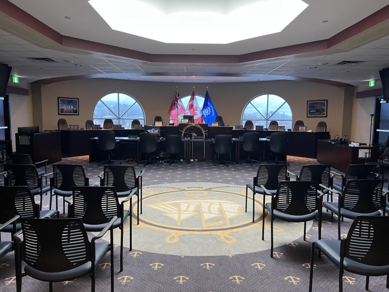 Council chamber with empty chairs, flags, and a circular decorative floor design.